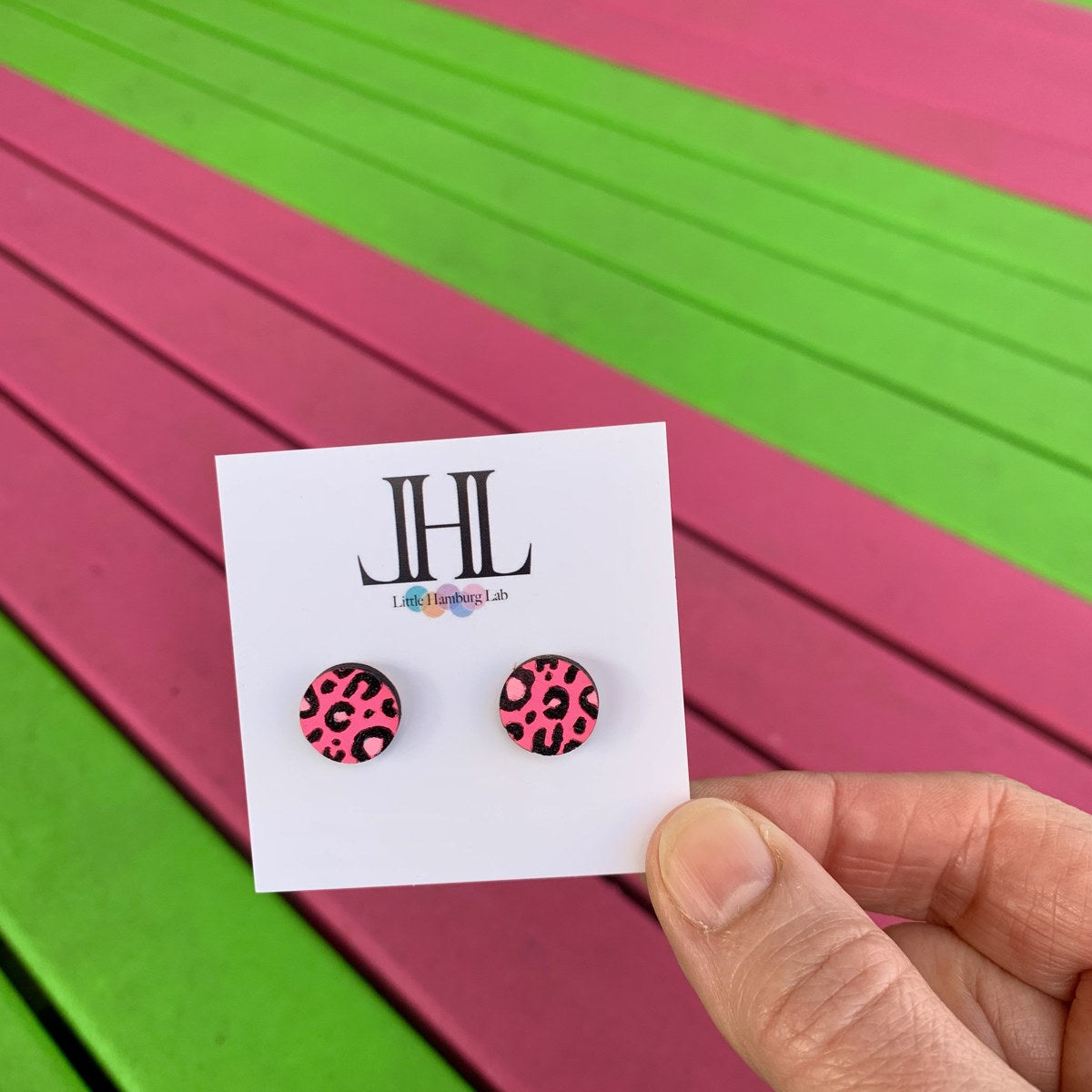 Pinke Leo-Ohrstecker aus Holz vor einer pink-grünen Bank