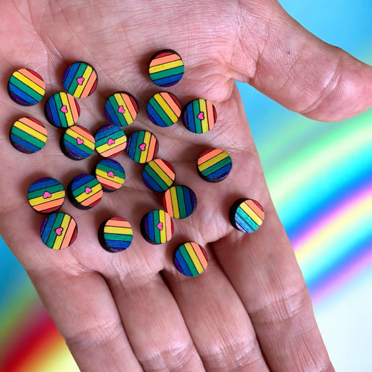 Viele Regenbogen-Ohrstecker aus Holz auf einer Hand, teils mit pinkem Herz
