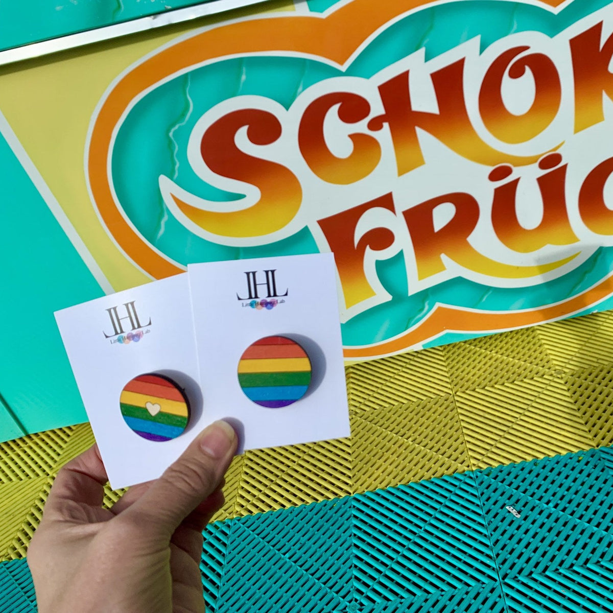 Regenbogen-Brosche und Ohrstecker vor buntem Schild