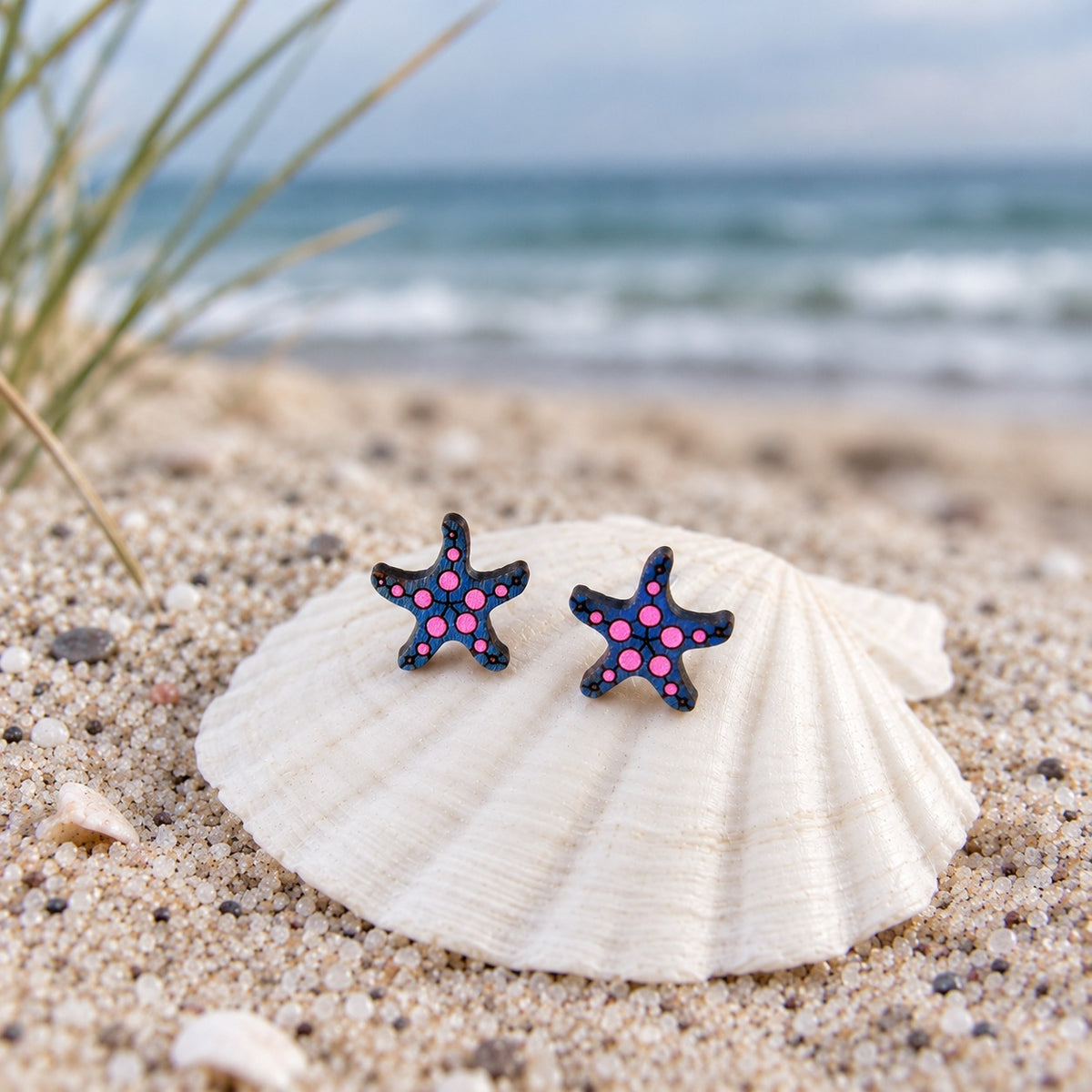 Seestern-Ohrstecker aus Holz in Marine mit neonpinken Punkten auf einer Muschel am Strand