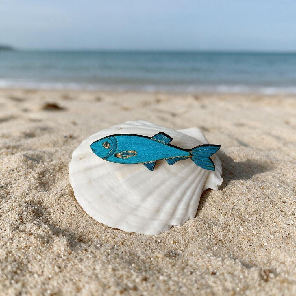 Blaue Sprotten-Brosche aus Holz auf einer Muschel am Strand