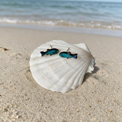 Blaue Sprotten-Ohrstecker aus Holz auf einer Muschel am Strand