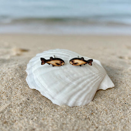 Sprotten-Ohrstecker aus Holz in Natur auf einer Muschel am Strand