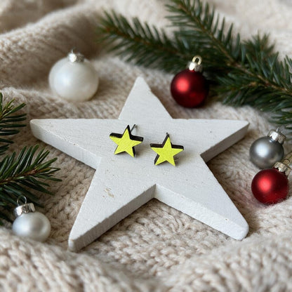 Sterne-Ohrstecker aus Holz in Neongelb auf einem weißen Holzstern mit Christbaumkugeln